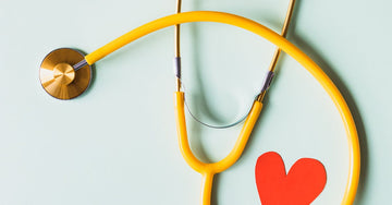 Medical stethoscope with red paper heart on white surface