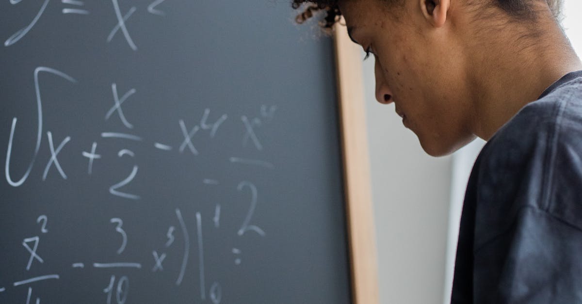 Side view of African American learner making math calculations on blackboard during lesson in classroom