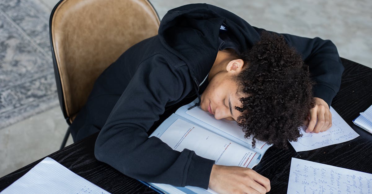 High angle of exhausted African American student resting on opened textbook and papers while preparing for exam